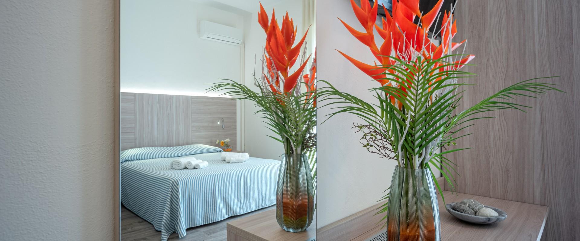 Camera moderna con letto matrimoniale, fiori arancioni in vaso e decorazioni naturali.