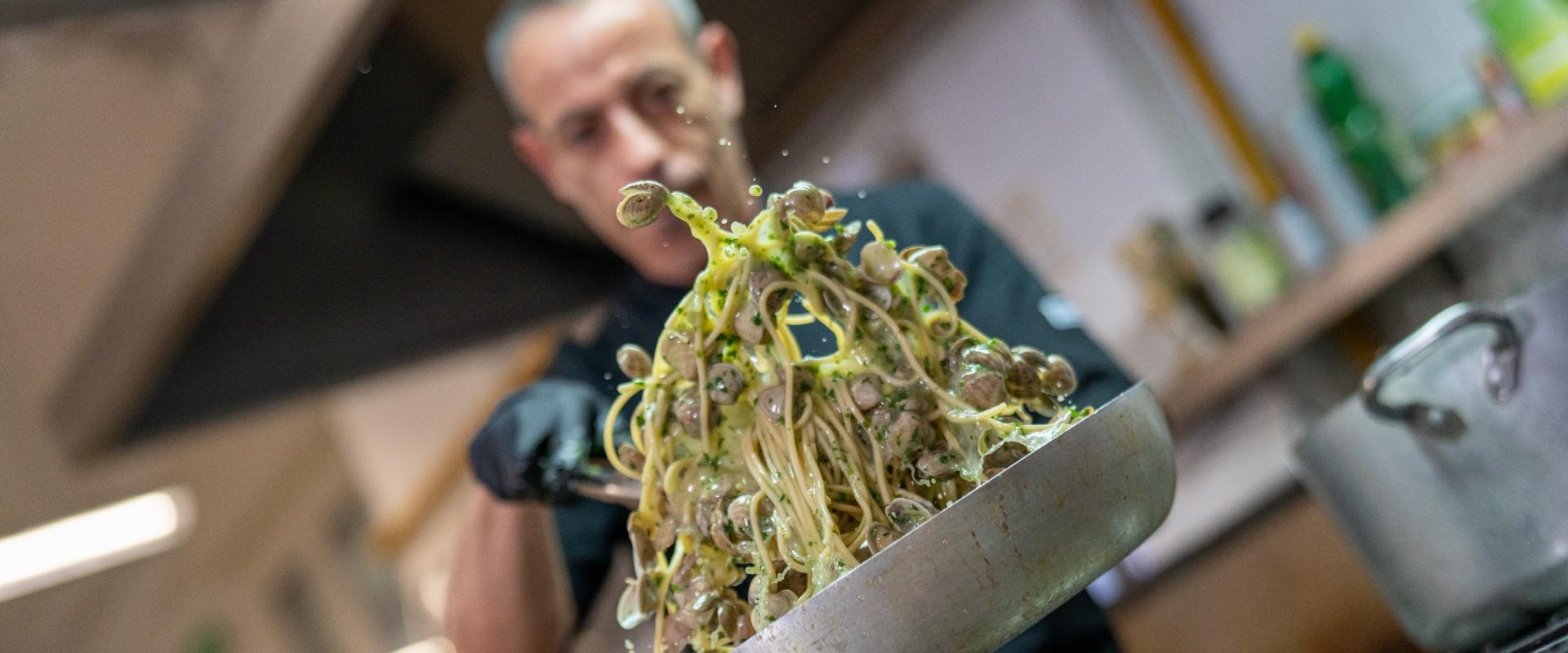 Chef cucina spaghetti con vongole e prezzemolo in una padella.