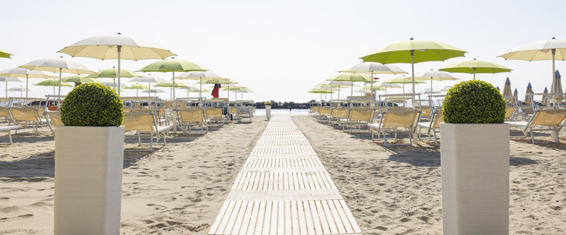 Beach with green umbrellas and sunbeds, walkway in the center.