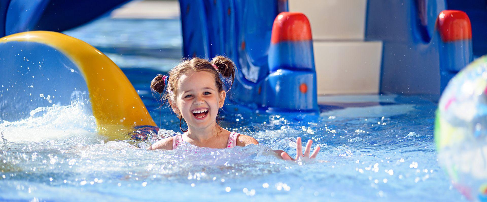 Bambina felice che gioca in piscina con uno scivolo.