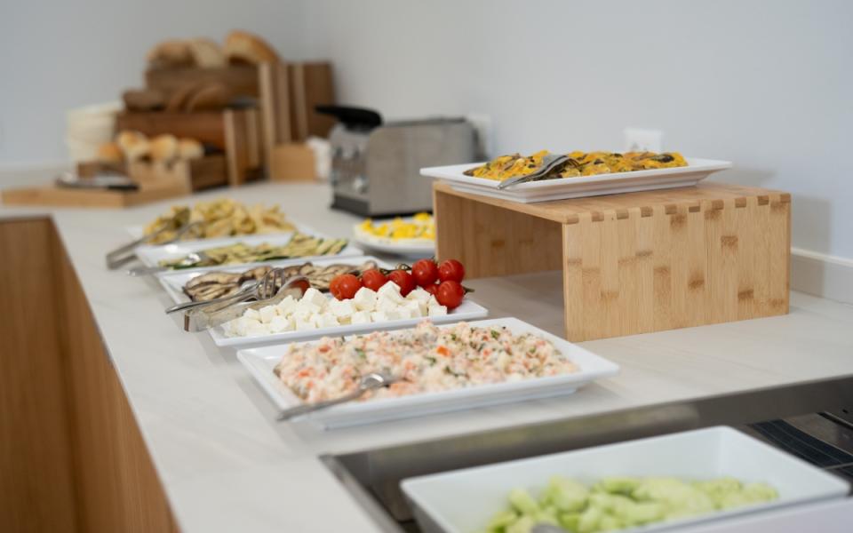 Buffet con verdure, formaggi e insalate su piatti bianchi, pane sullo sfondo.