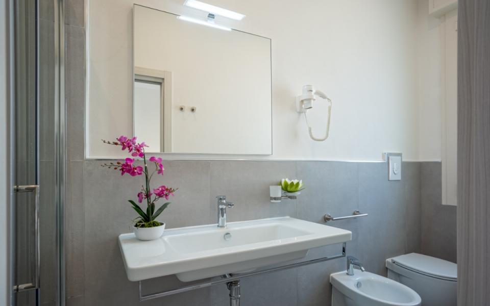 Bagno moderno con lavabo, specchio, bidet, WC e pianta decorativa.