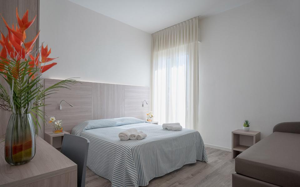 Camera moderna con letto matrimoniale, fiori vivaci e luce naturale, atmosfera accogliente.