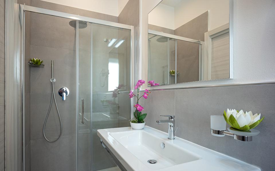Bagno moderno con doccia in vetro, lavabo bianco e decorazioni floreali.