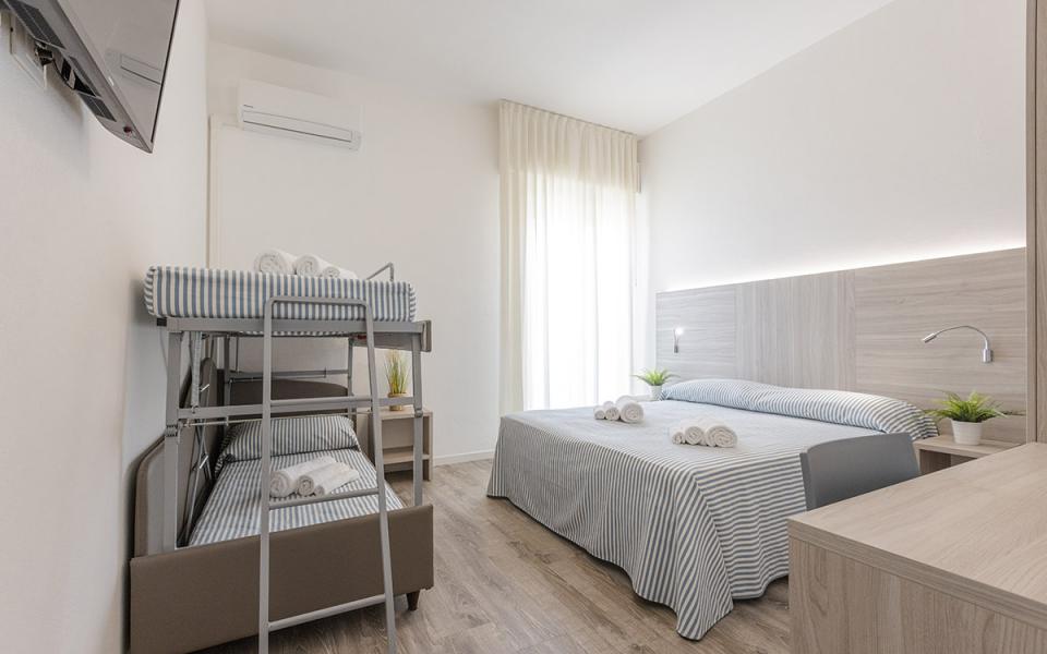 Camera moderna con letto matrimoniale e letti a castello, arredamento minimalista e luminoso.