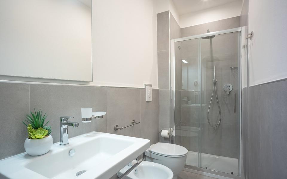Bagno moderno con doccia, lavabo, bidet e decorazione vegetale.