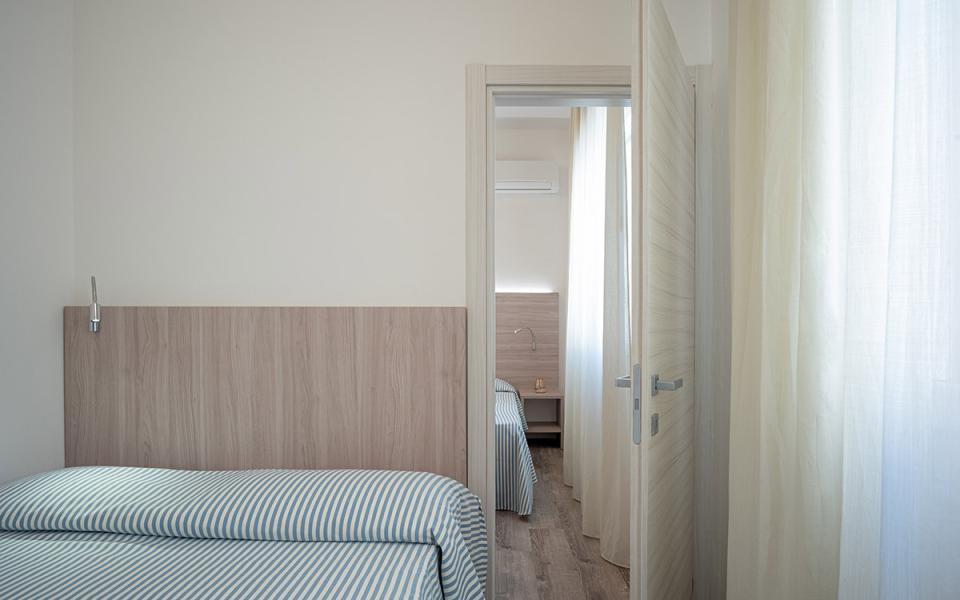 Camera con letto a righe, porta aperta e luce naturale dalle tende.