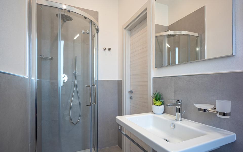 Bagno moderno con doccia in vetro, lavabo bianco e specchio.