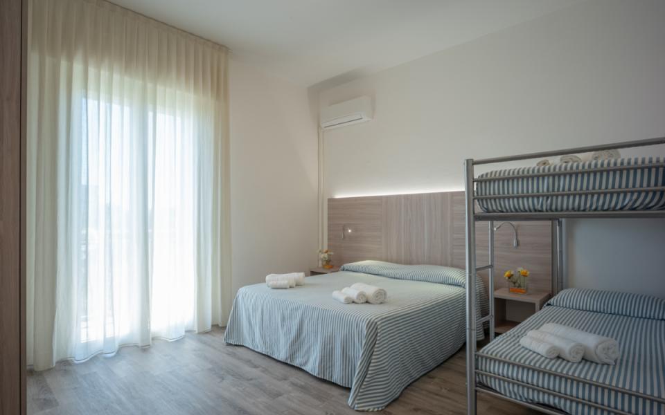Camera luminosa con letto matrimoniale e letti a castello, arredamento moderno e minimalista.
