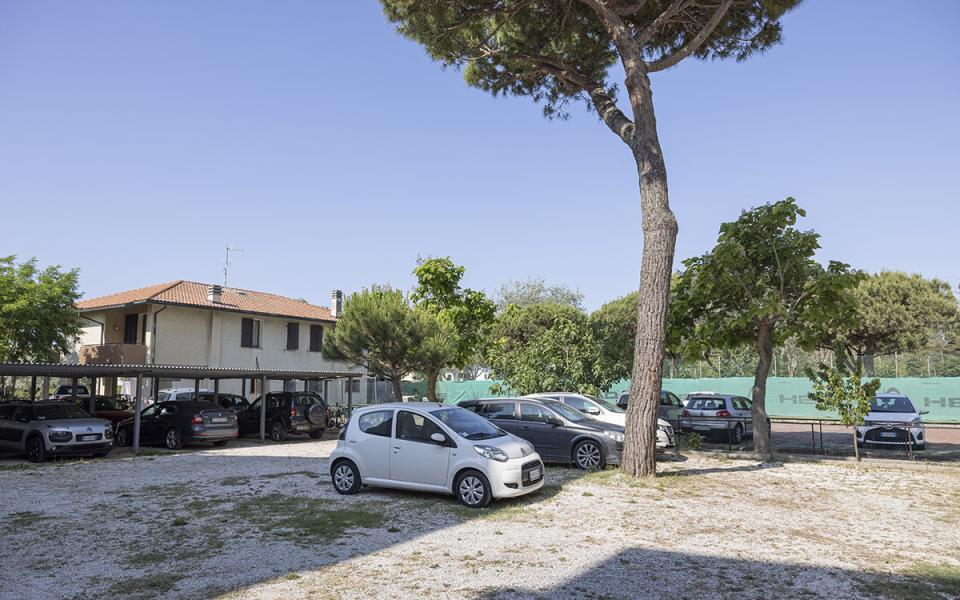 Parcheggio all'aperto con auto e alberi, vicino a una casa con tetto rosso.