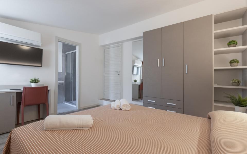 Camera moderna con letto, armadio, scrivania e bagno adiacente.