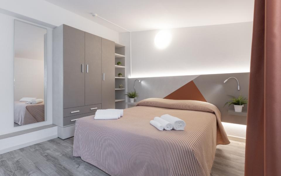 Camera moderna con letto matrimoniale, armadio grigio e decorazioni geometriche.