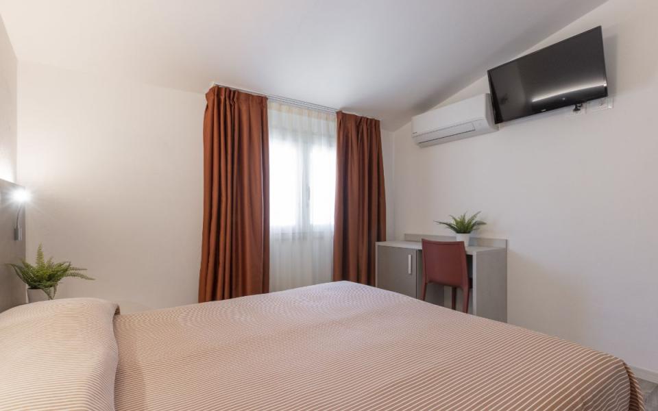 Camera moderna con letto, TV, scrivania e tende marroni.