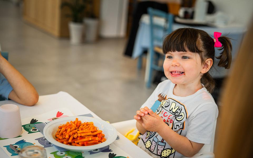 Bambina sorridente con pasta al pomodoro in un ristorante.