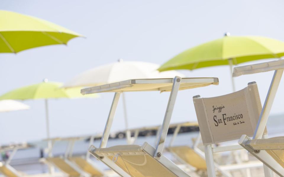 Spiaggia con lettini e ombrelloni verdi e bianchi, atmosfera rilassante e soleggiata.