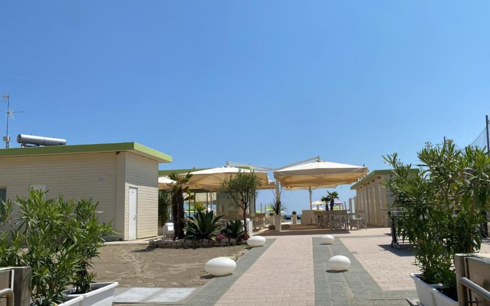 Spiaggia con ombrelloni bianchi, piante e cielo limpido in una giornata soleggiata.