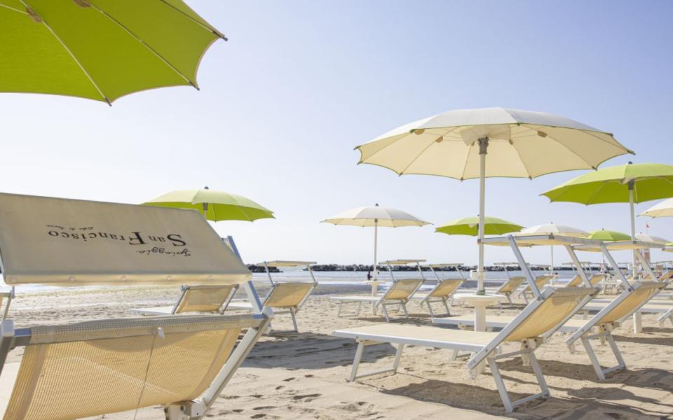 Spiaggia con ombrelloni e lettini, cielo sereno e mare calmo in lontananza.